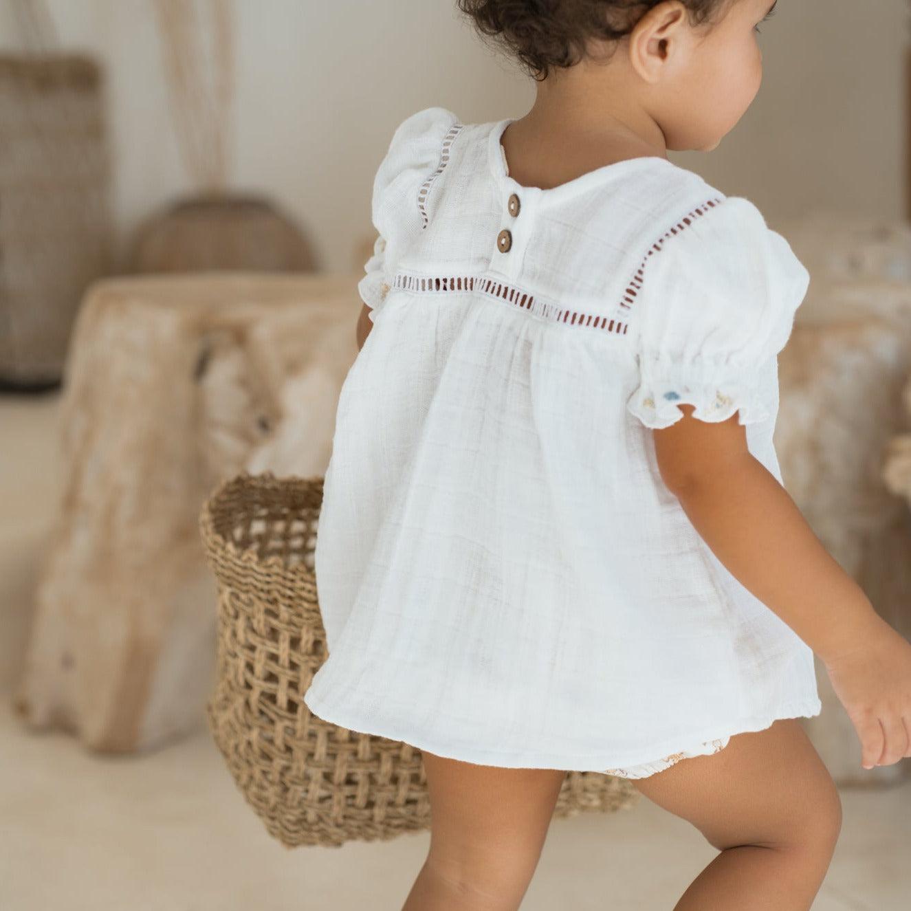 A vintage-inspired Illoura the Label baby girl in a white cotton clover blouse & bloomer set and basket.