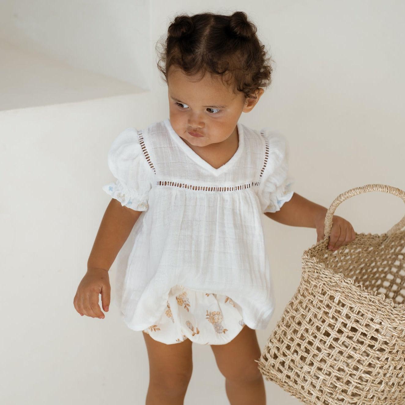 A vintage-inspired little girl wearing the Illoura the Label clover blouse & bloomer set and holding a basket.