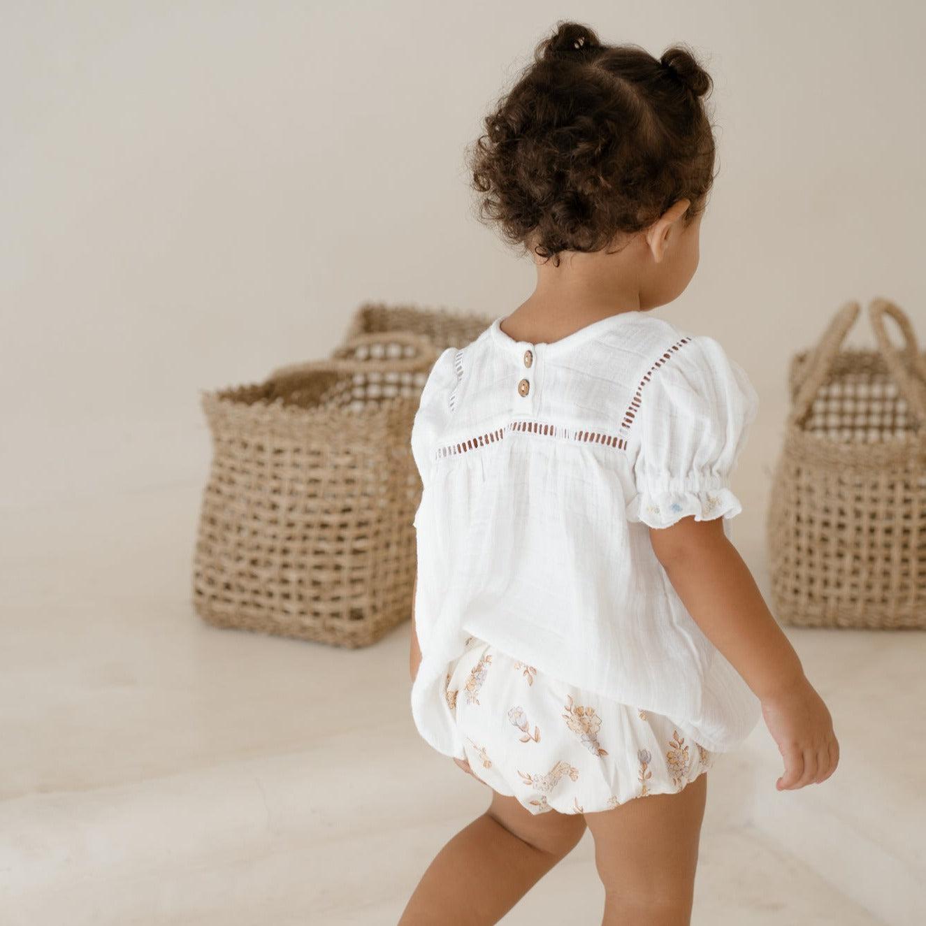 A little girl wearing a vintage-inspired Illoura the Label clover blouse & bloomer set and carrying a basket.
