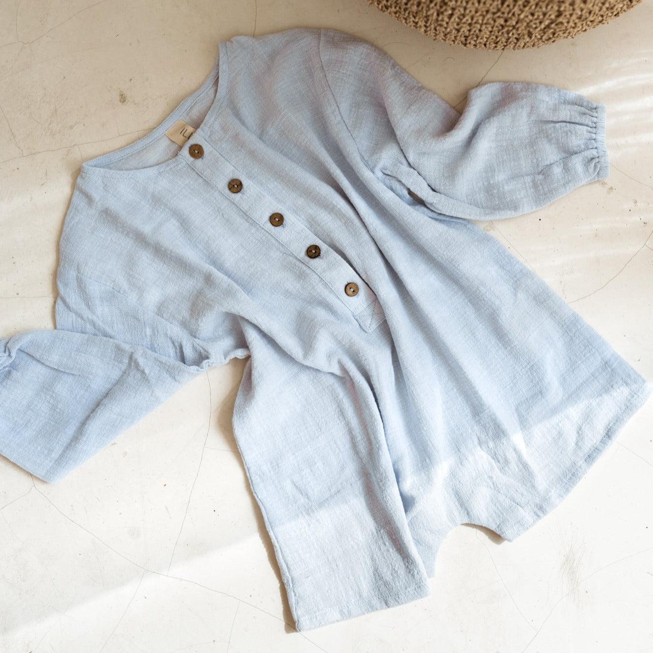 An Illoura the Label husk romper in powder blue with buttons and a basket on the floor.