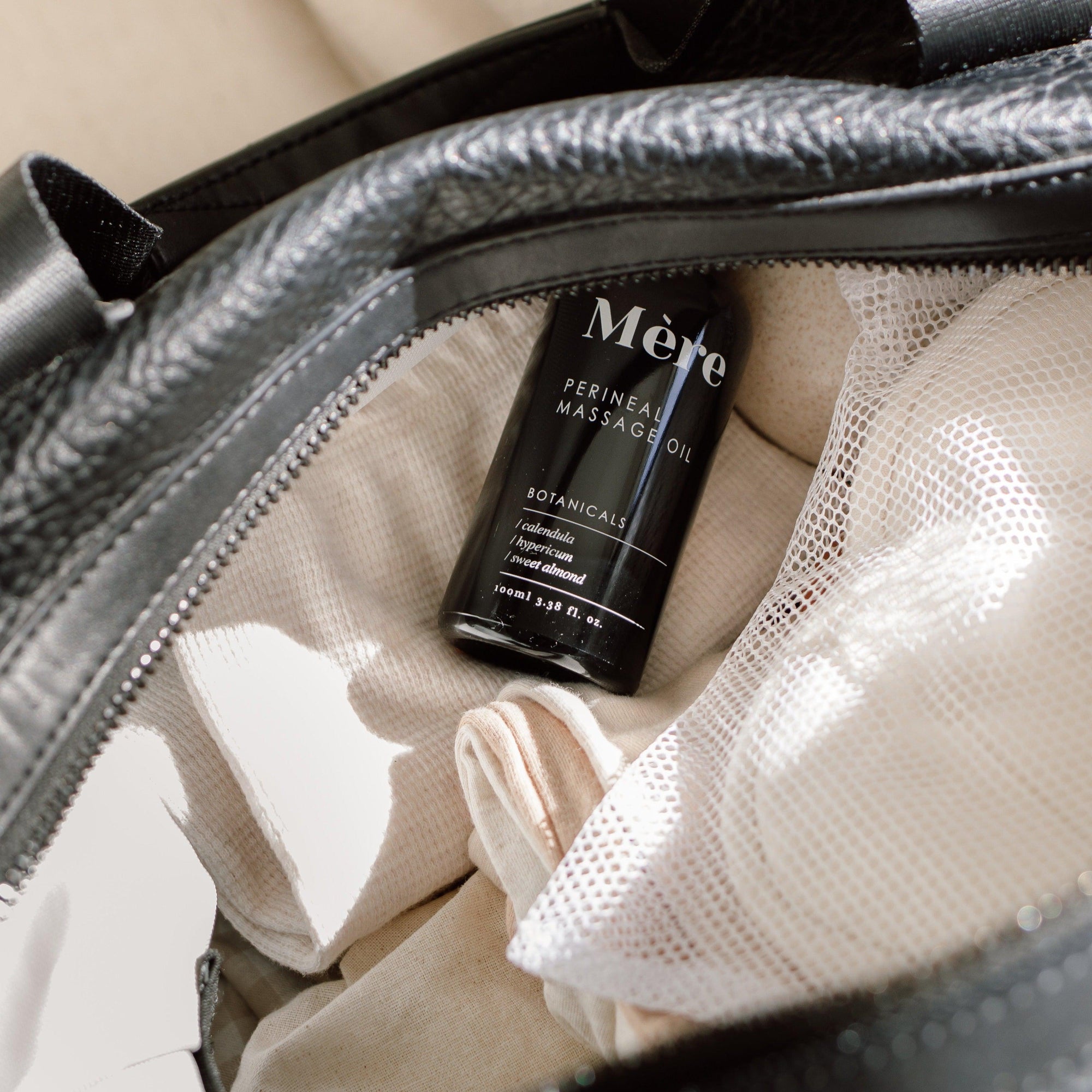 A black bag containing a bottle of Mère Perineal Massage Oil.