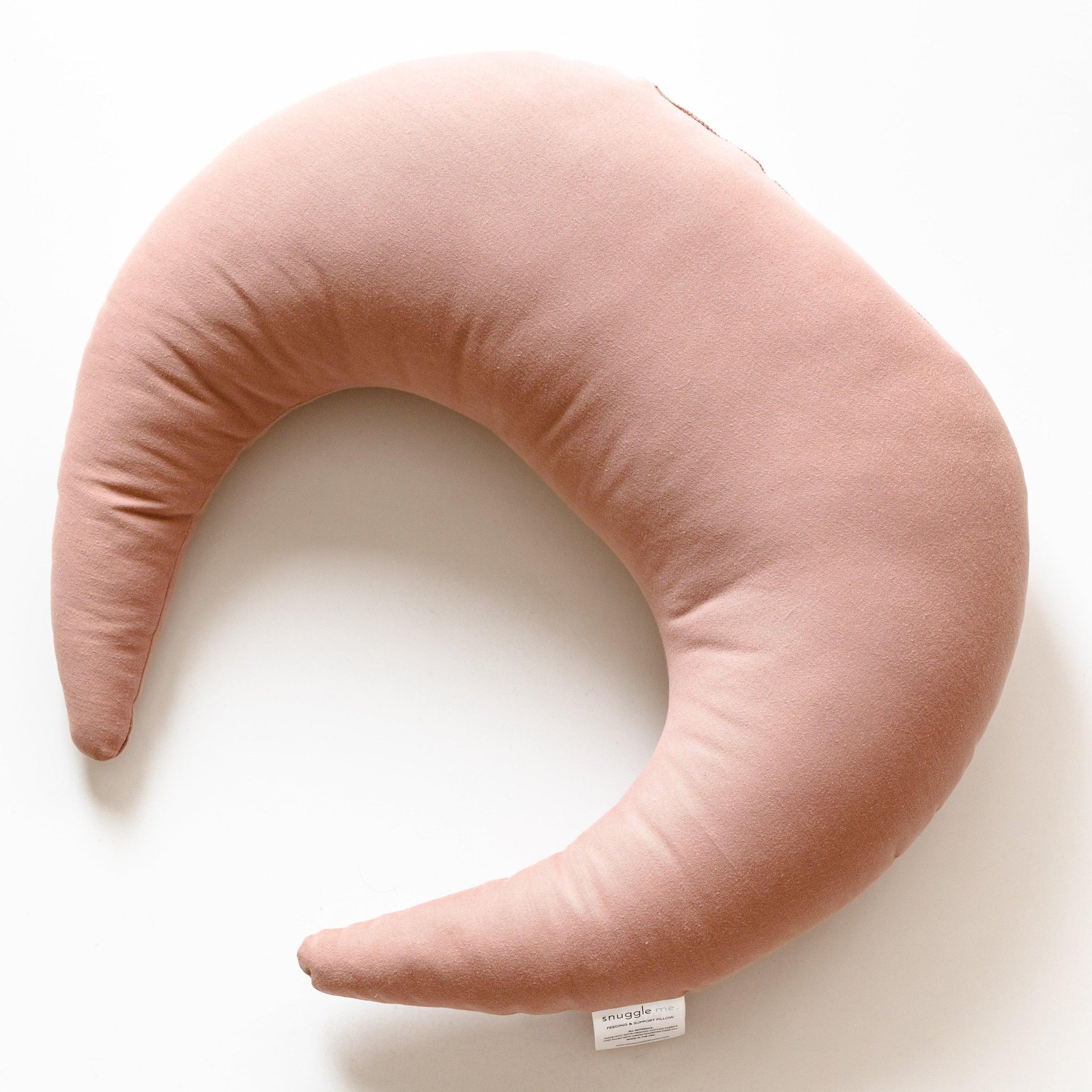 A pink crescent-shaped Feeding & Support Pillow by Gumdrop on a white surface.