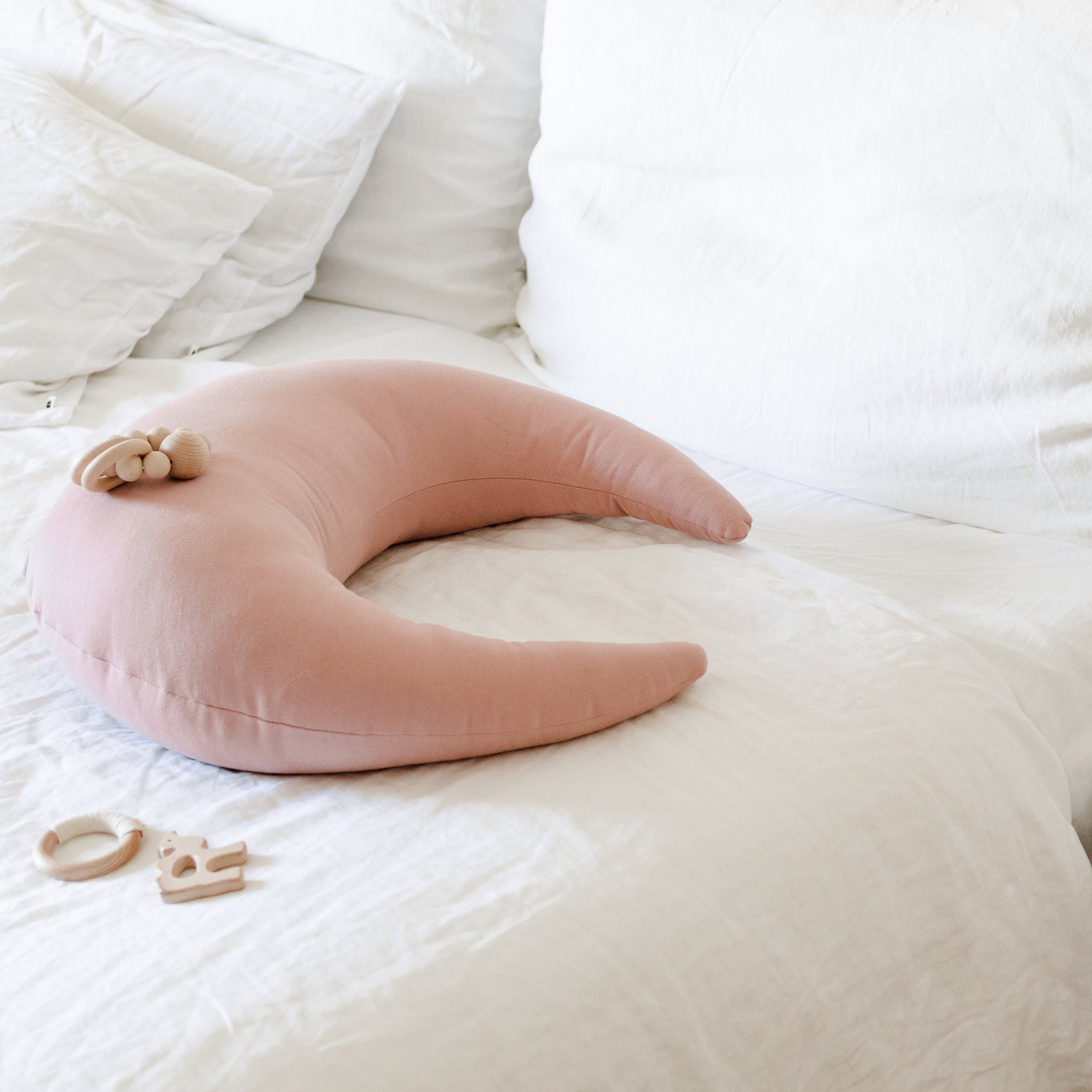 A crescent-shaped Feeding & Support Pillow by Snuggle Me in the shade Gumdrop on a bed.