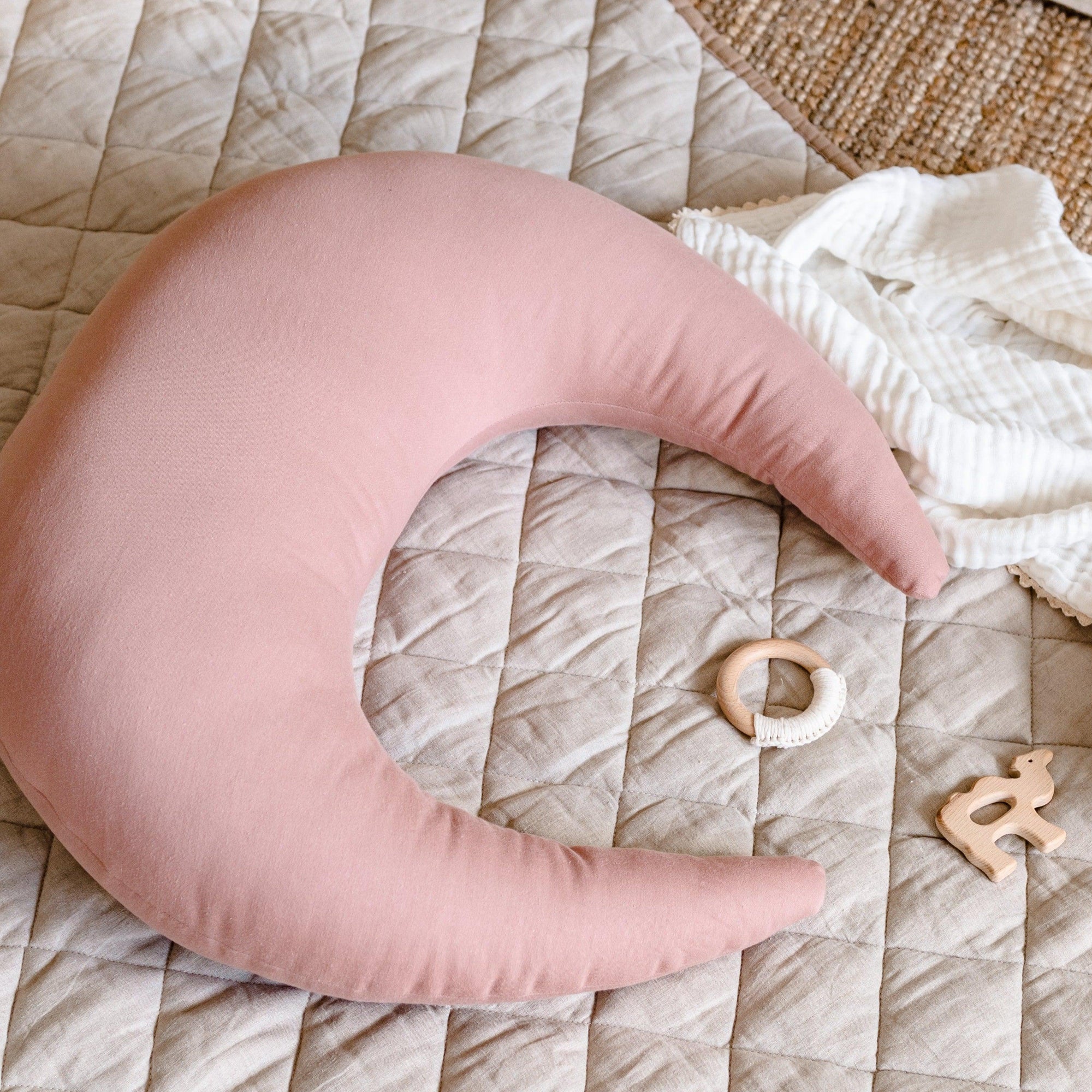 A crescent-shaped Feeding & Support Pillow by Snuggle Me in the shade Gumdrop on a baby mat.