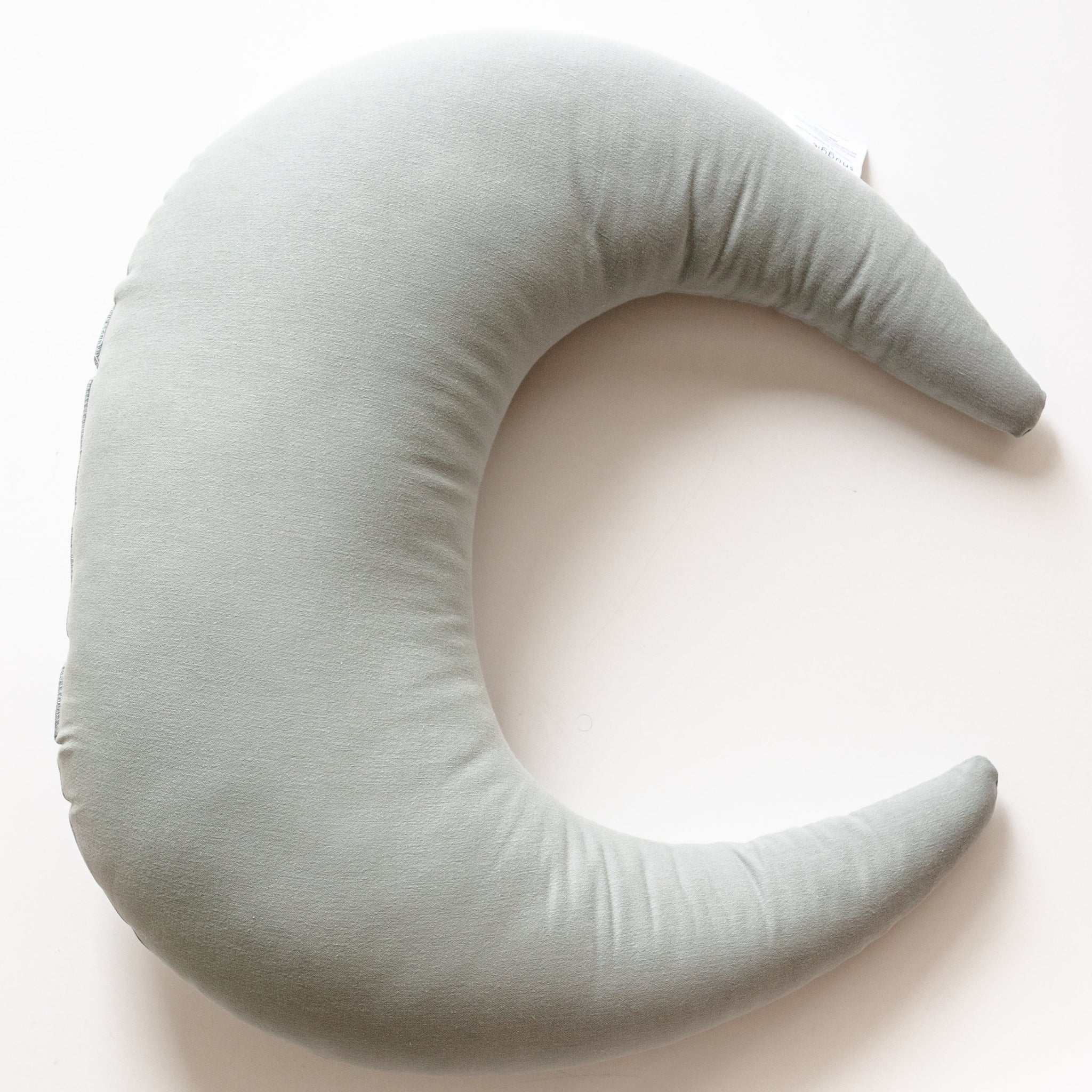 A Snuggle Me Feeding & Support Pillow in a crescent shape in the shade Slate on a white surface.