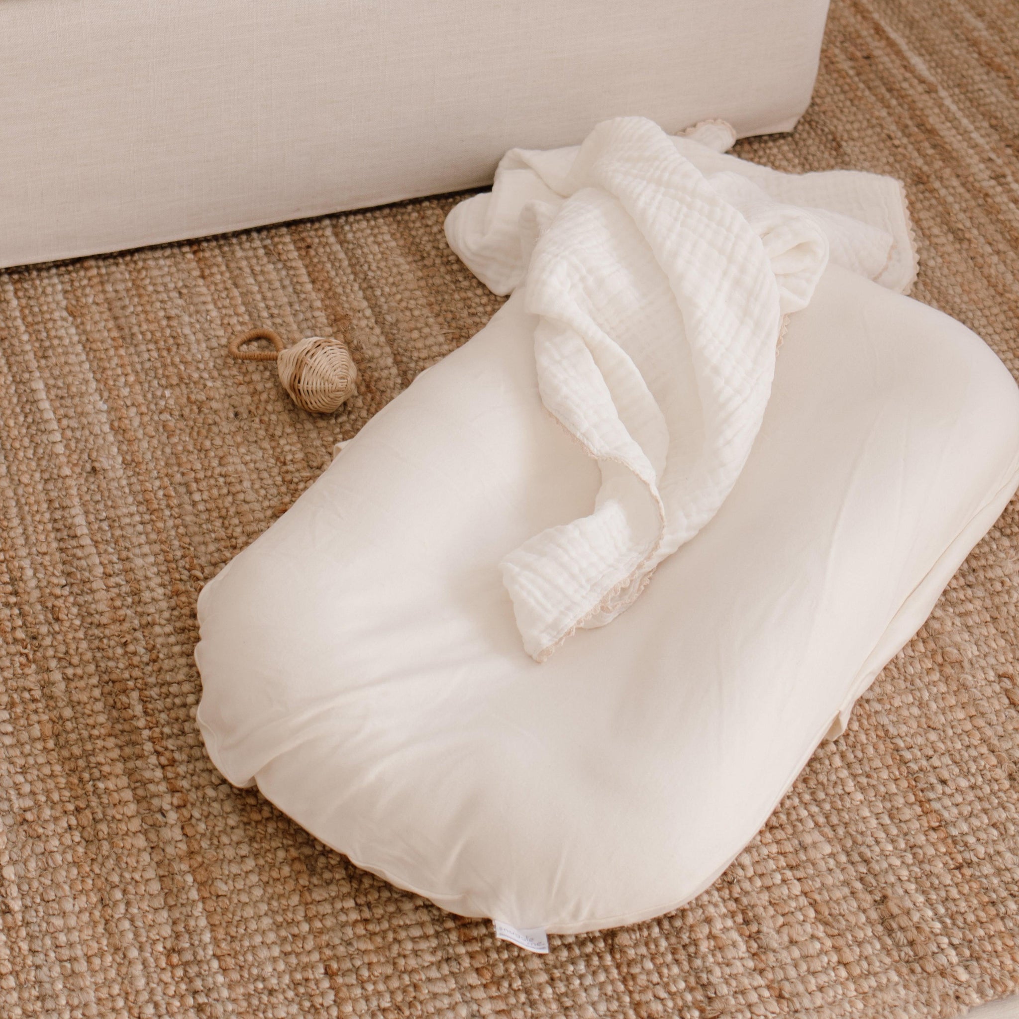 The Snuggle Me® Lounger on a woven rug with a white blanket on top.