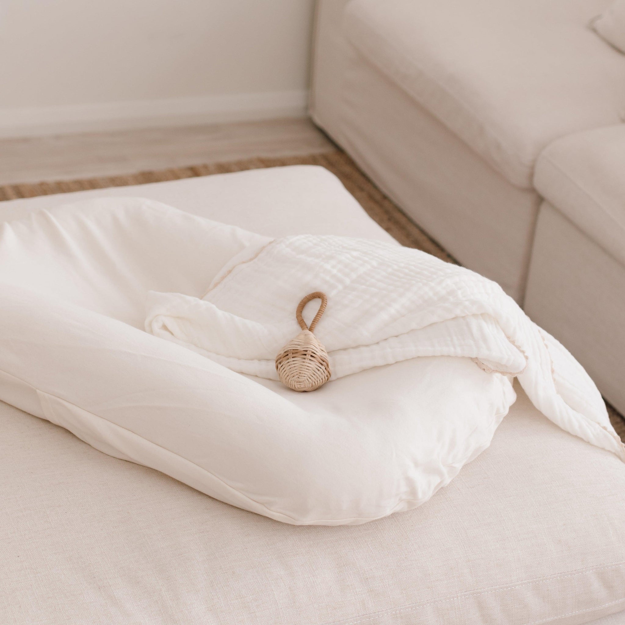 The Snuggle Me® Lounger on a woven rug with a white blanket on top next to a lounge.
